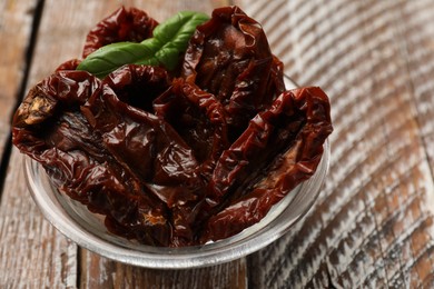 Photo of Delicious sun dried tomatoes with basil in glass bowl on wooden table, closeup