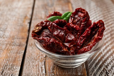 Photo of Delicious sun dried tomatoes with basil in glass bowl on wooden table, closeup. Space for text
