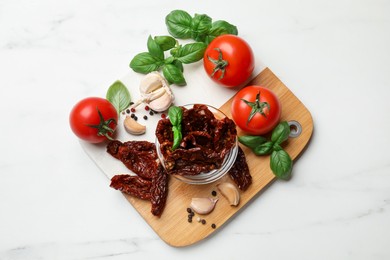 Photo of Delicious sun dried tomatoes, fresh vegetables and spices on white marble table, top view
