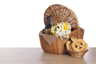 Photo of Picnic wicker basket with beautiful flowers, bottle of wine and pretzels on wooden table against white background, closeup. Space for text