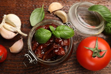 Photo of Delicious sun dried tomatoes in glass jar, fresh vegetables and spices on wooden table, flat lay