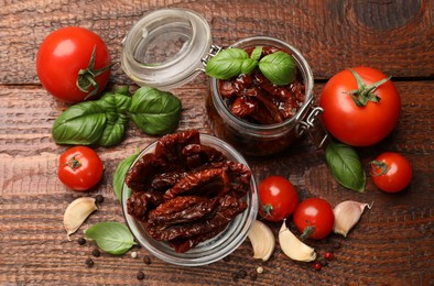 Photo of Delicious sun dried tomatoes in glass dishware, fresh vegetables and spices on wooden table, flat lay