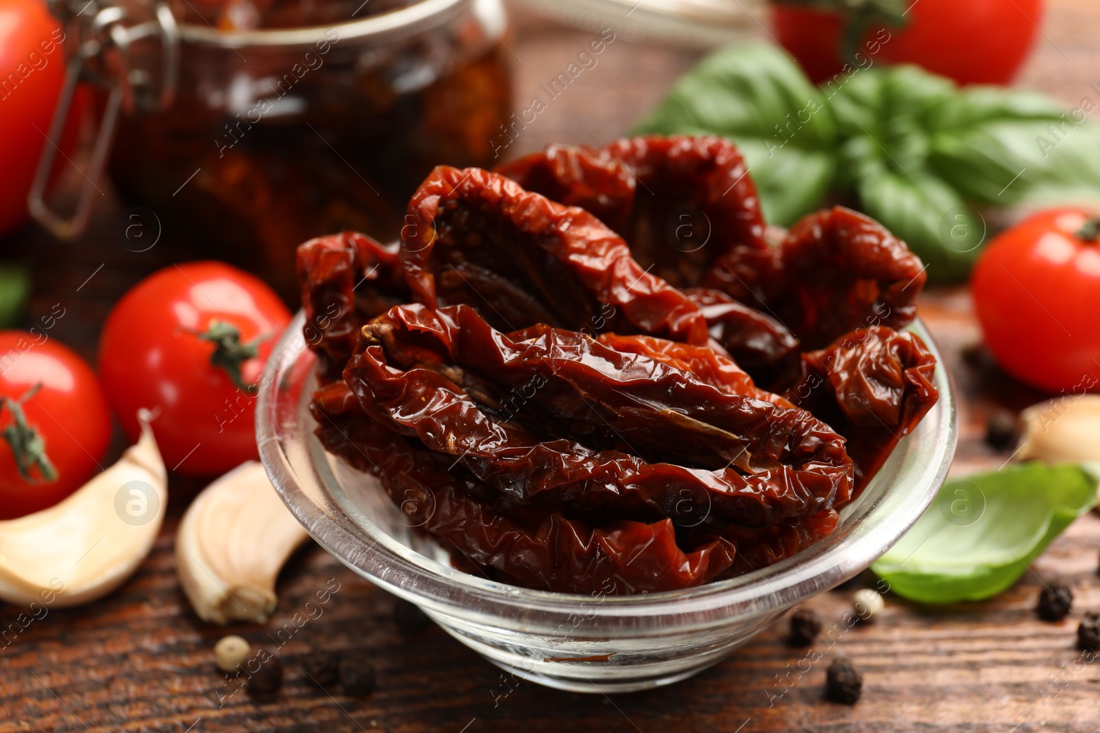 Delicious sun dried tomatoes in glass bowl, fresh vegetables and spices on wooden table, closeup Photo of Delicious sun dried tomatoes in glass bowl, fresh vegetables and spices on wooden table, closeup