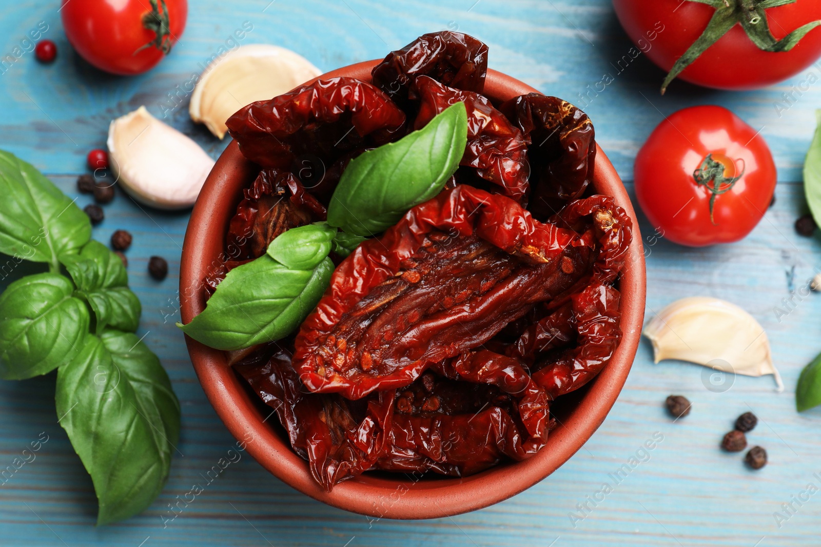 Delicious sun dried tomatoes in bowl, fresh vegetables and spices on light blue wooden table, flat lay Photo of Delicious sun dried tomatoes in bowl, fresh vegetables and spices on light blue wooden table, flat lay