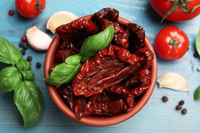 Photo of Delicious sun dried tomatoes in bowl, fresh vegetables and spices on light blue wooden table, flat lay