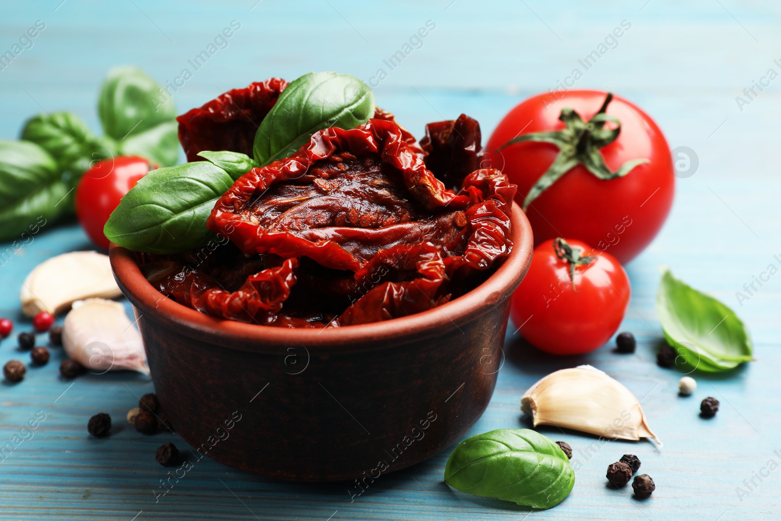 Delicious sun dried tomatoes in bowl, fresh vegetables and spices on light blue wooden table, closeup Photo of Delicious sun dried tomatoes in bowl, fresh vegetables and spices on light blue wooden table, closeup