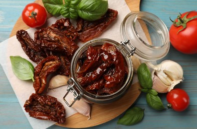 Photo of Delicious sun dried tomatoes in glass jar, fresh vegetables and spices on light blue wooden table, flat lay