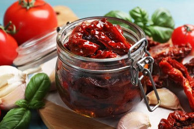 Photo of Delicious sun dried tomatoes in glass jar, fresh vegetables and spices on table, closeup