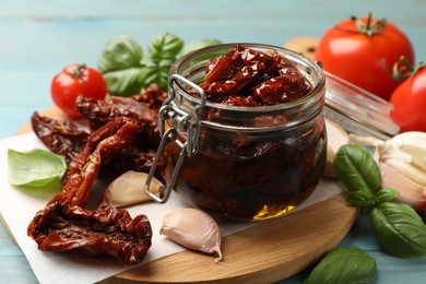 Photo of Delicious sun dried tomatoes in glass jar, fresh vegetables and spices on light blue table, closeup