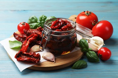 Photo of Delicious sun dried tomatoes in glass jar, fresh vegetables and spices on light blue wooden table, closeup