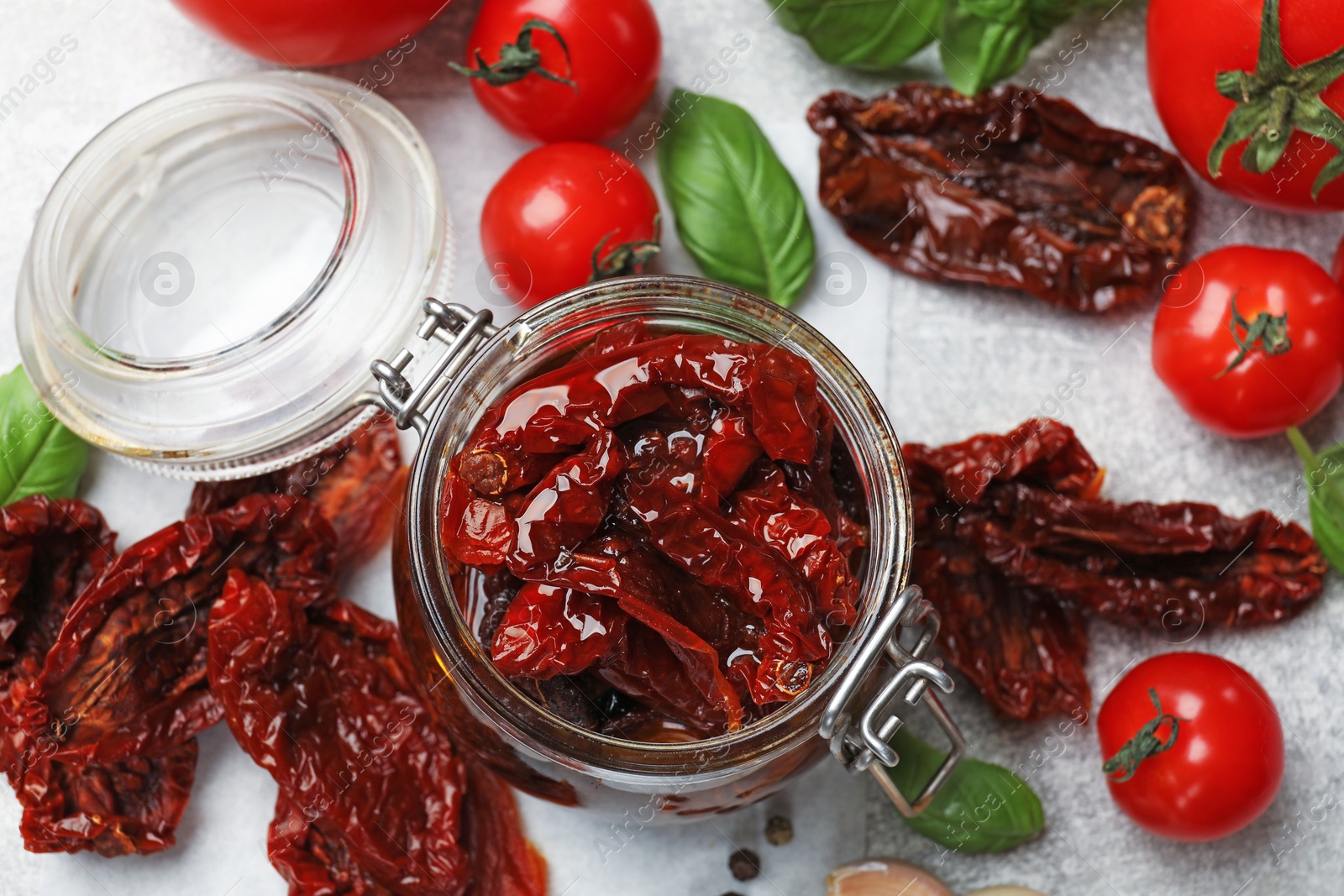 Delicious sun dried tomatoes in glass jar, fresh vegetables and basil on gray table, flat lay Photo of Delicious sun dried tomatoes in glass jar, fresh vegetables and basil on gray table, flat lay