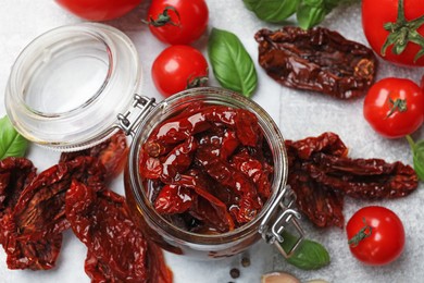 Photo of Delicious sun dried tomatoes in glass jar, fresh vegetables and basil on gray table, flat lay