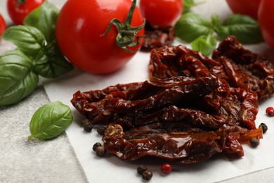 Photo of Delicious sun dried tomatoes, fresh vegetables and spices on gray textured table, closeup