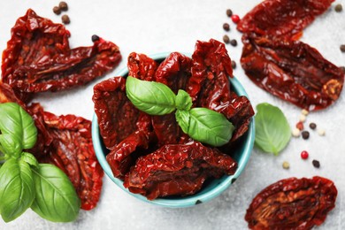 Photo of Delicious sun dried tomatoes in bowl and spices on gray table, flat lay