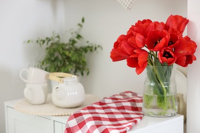 Photo of Beautiful red tulips in vase, cups and teapot on cabinet indoors