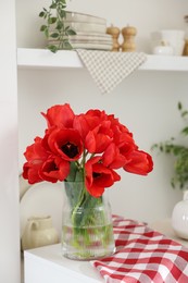Photo of Beautiful red tulips in vase on cabinet indoors