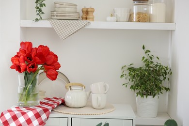 Photo of Beautiful red tulips in vase, cups and teapot on cabinet indoors