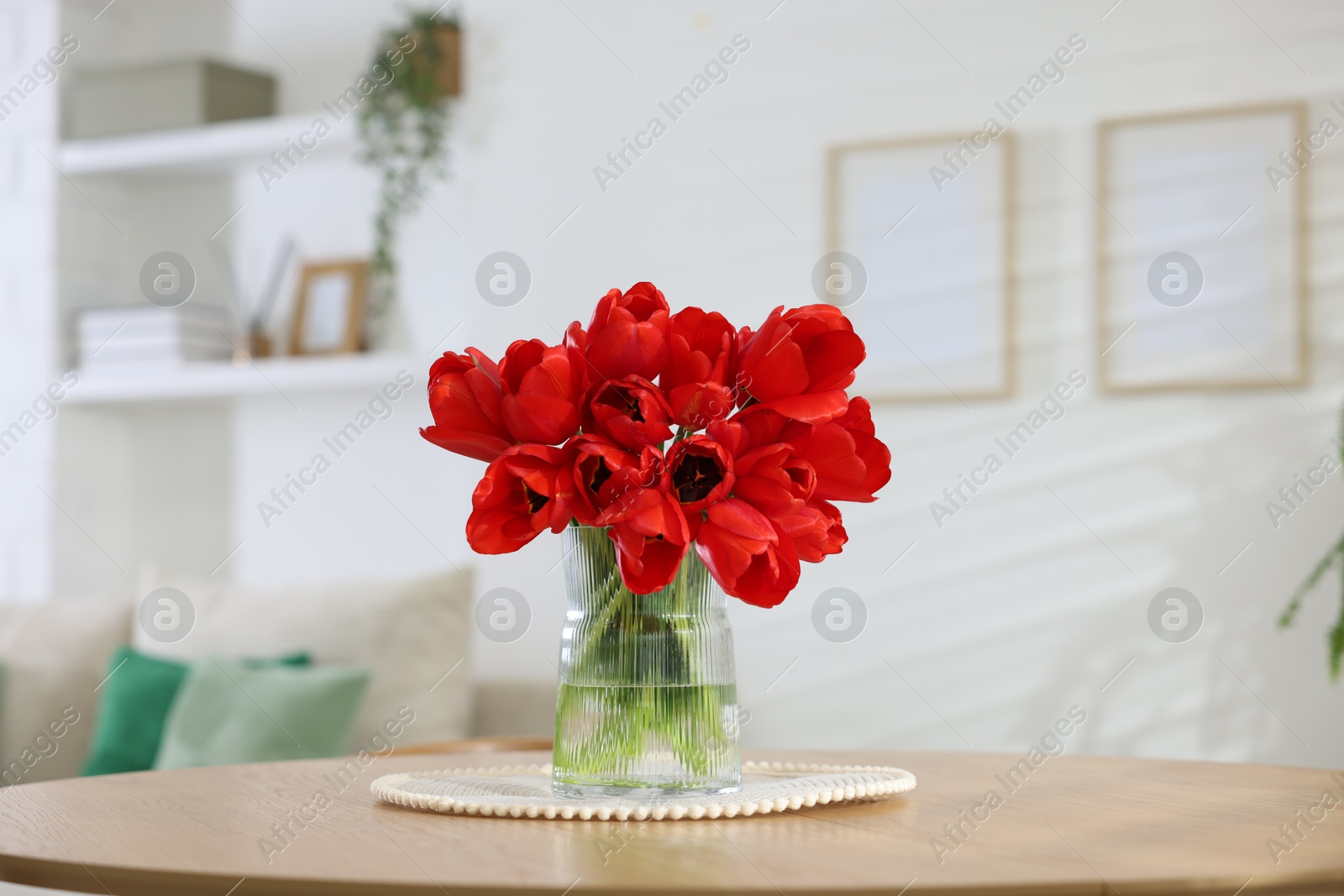 Photo of Beautiful red tulips in vase on wooden table indoors