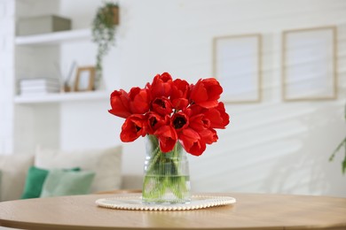 Photo of Beautiful red tulips in vase on wooden table indoors