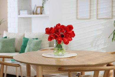 Photo of Beautiful red tulips in vase on wooden table indoors