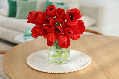 Photo of Beautiful red tulips in vase on wooden table indoors