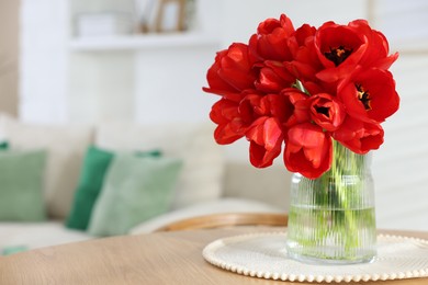 Photo of Beautiful red tulips in vase on wooden table indoors, space for text