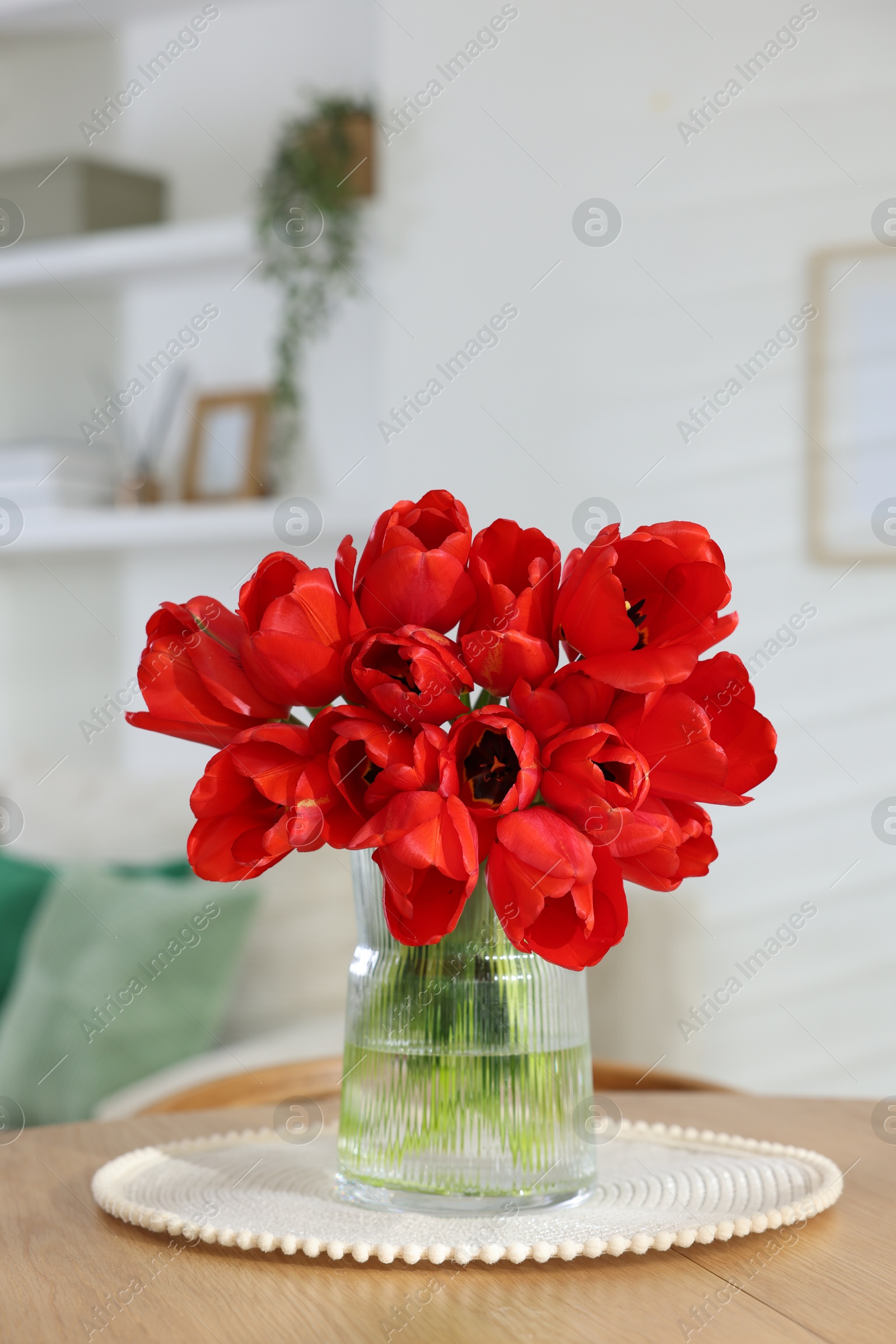 Photo of Beautiful red tulips in vase on wooden table indoors