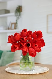 Photo of Beautiful red tulips in vase on wooden table indoors