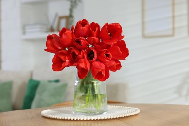 Photo of Beautiful red tulips in vase on wooden table indoors
