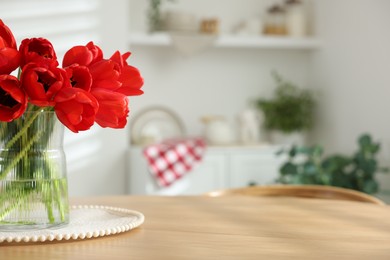 Photo of Beautiful red tulips in vase on wooden table indoors, closeup. Space for text