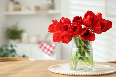 Photo of Beautiful red tulips in vase on wooden table indoors, space for text