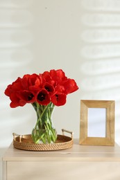 Photo of Beautiful red tulips in vase and frame on cabinet indoors