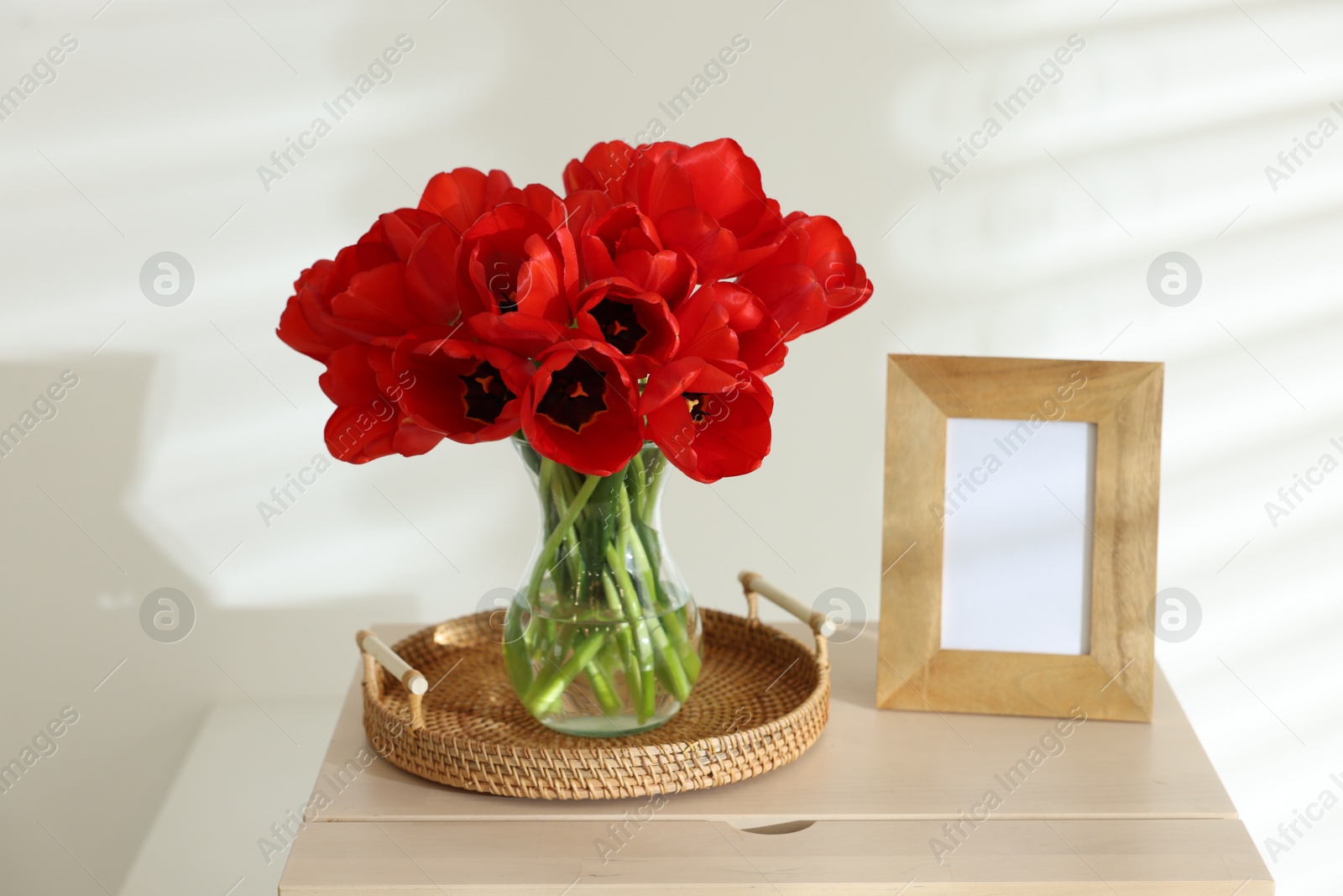 Photo of Beautiful red tulips in vase and frame on cabinet indoors