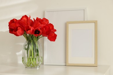 Photo of Beautiful red tulips in vase and frames on white table indoors