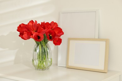 Photo of Beautiful red tulips in vase and frames on white table indoors