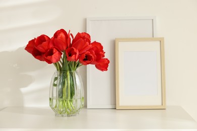 Photo of Beautiful red tulips in vase and frames on white table indoors