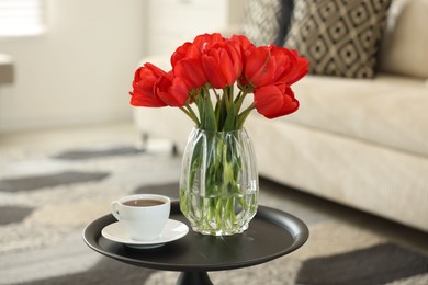 Photo of Beautiful red tulips in vase and tea on table indoors
