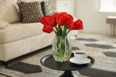 Photo of Beautiful red tulips in vase and tea on table indoors, space for text