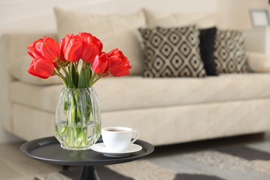 Photo of Beautiful red tulips in vase and tea on table indoors, space for text
