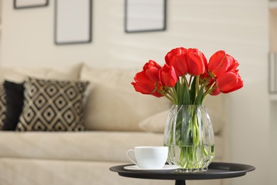 Photo of Beautiful red tulips in vase and tea on table indoors, space for text