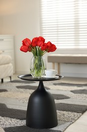 Photo of Beautiful red tulips in vase and tea on table indoors