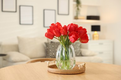 Photo of Beautiful red tulips in vase on wooden table indoors