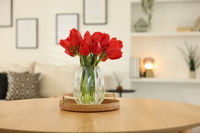 Photo of Beautiful red tulips in vase on wooden table indoors