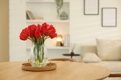 Photo of Beautiful red tulips in vase on wooden table indoors, space for text