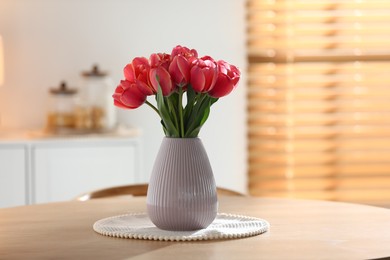 Photo of Beautiful tulips in vase on wooden table indoors