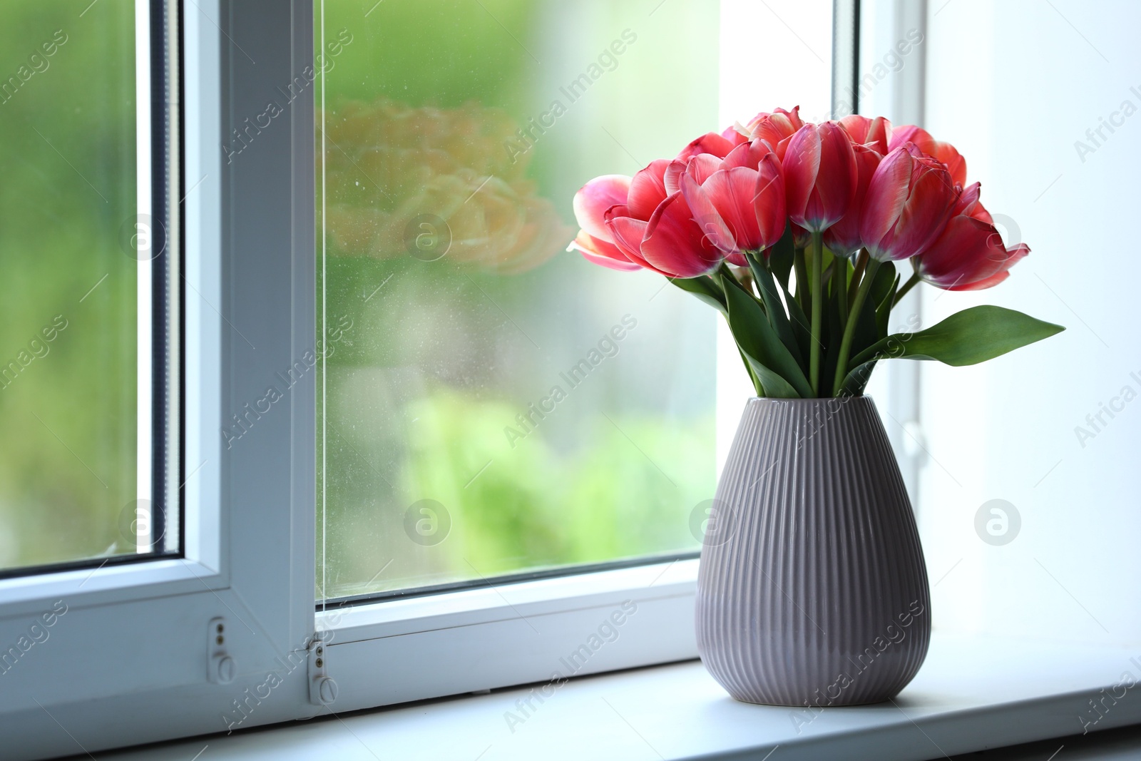 Photo of Beautiful tulips in vase on window sill. Space for text