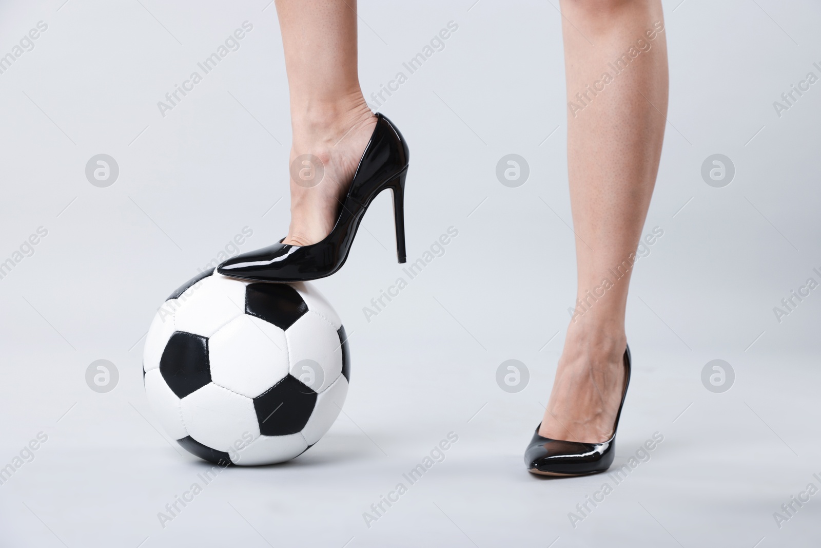 Photo of Woman in high heeled shoes with soccer ball on light background, closeup