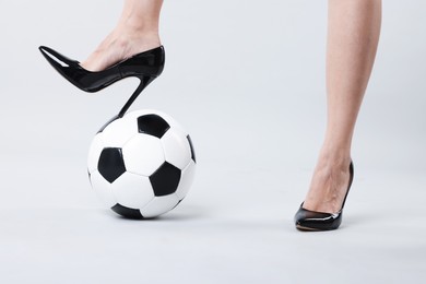 Photo of Woman in high heeled shoes with soccer ball on light background, closeup