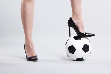 Photo of Woman in high heeled shoes with soccer ball on light background, closeup