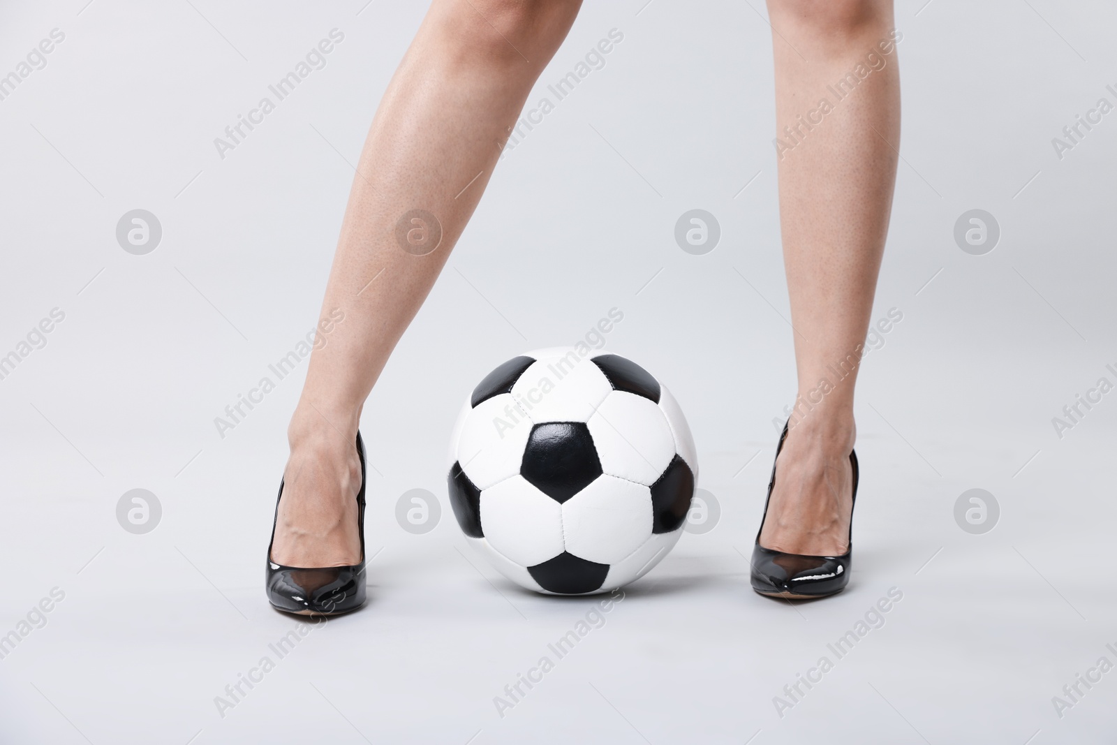 Photo of Woman in high heeled shoes with soccer ball on light background, closeup